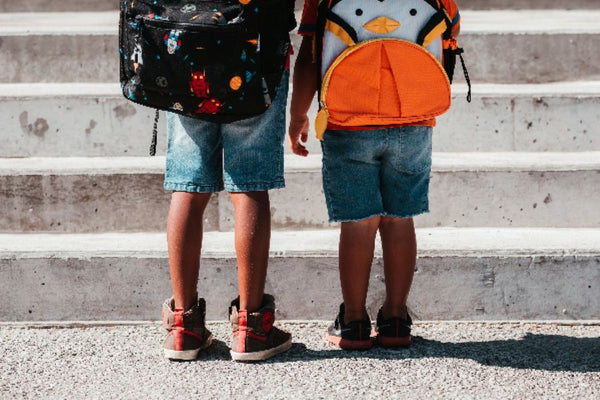 Children wearing bookbags standing at the bottom of steps.