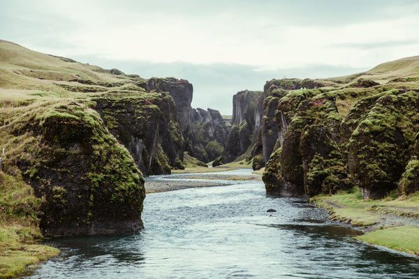Stream passing through cliffs covered in greenery.